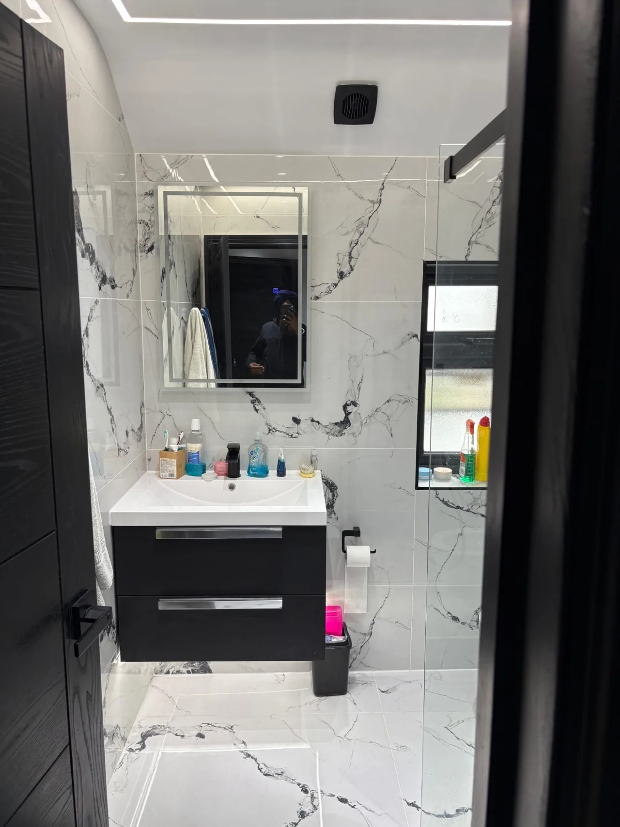 White basin above a dark vanity unit beside light stone-effect tiles